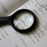 A magnifying glass focuses on mathematical equations in a textbook, highlighting detailed calculations.