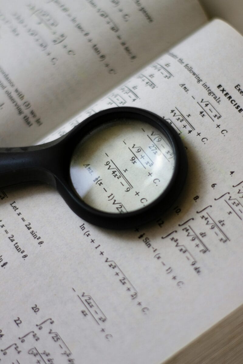 A magnifying glass focuses on mathematical equations in a textbook, highlighting detailed calculations.