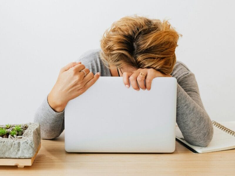 Woman showing fatigue resting head on laptop, workspace stress.